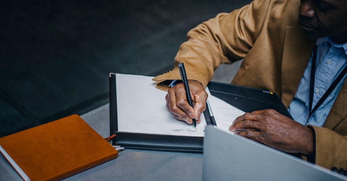 Two people writing in notebooks across a desk during a meeting