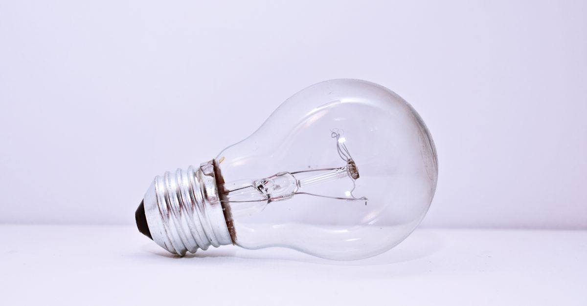 A single clear light bulb lying on a pale surface