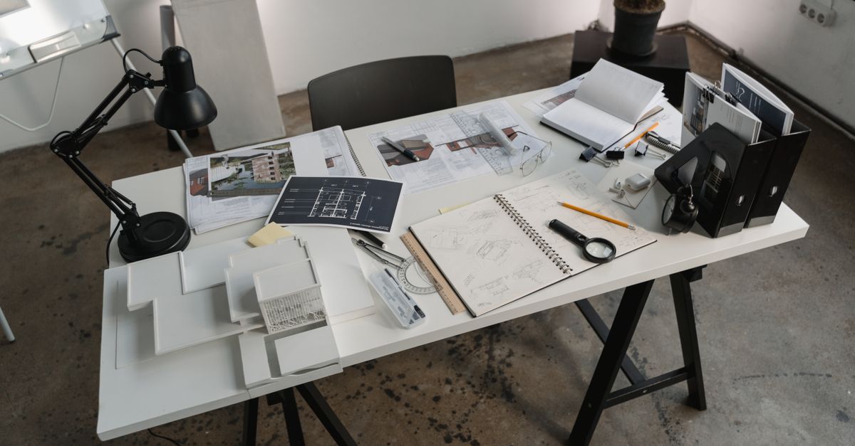 A tidy white desk with a lamp, notebooks and photographs laid out on it