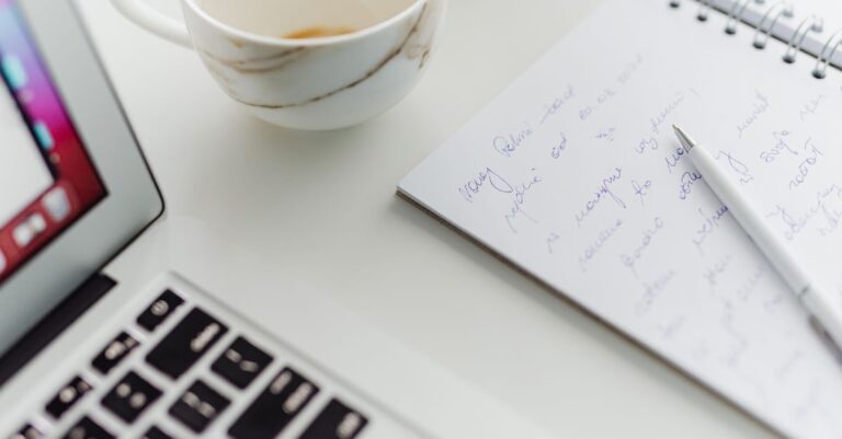 A handwritten notepad and a cup of coffee beside a laptop keyboard