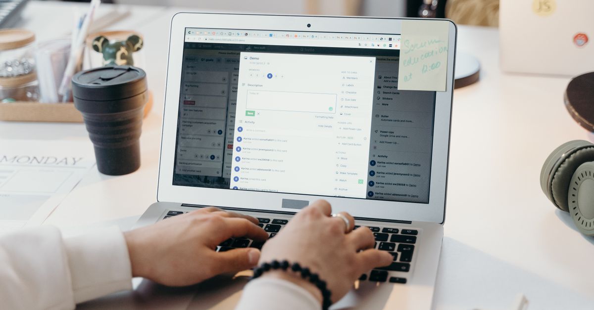 Hands typing on a laptop at a desk with a coffee cup and headphones