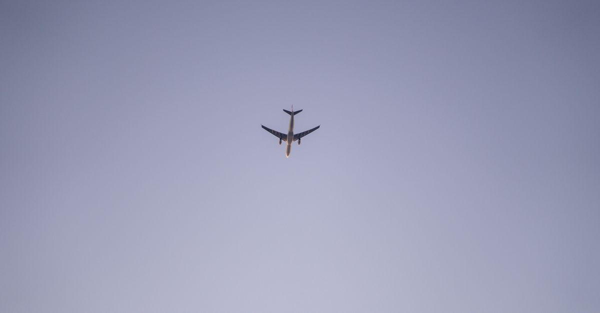A distant aeroplane flying across a clear pale sky
