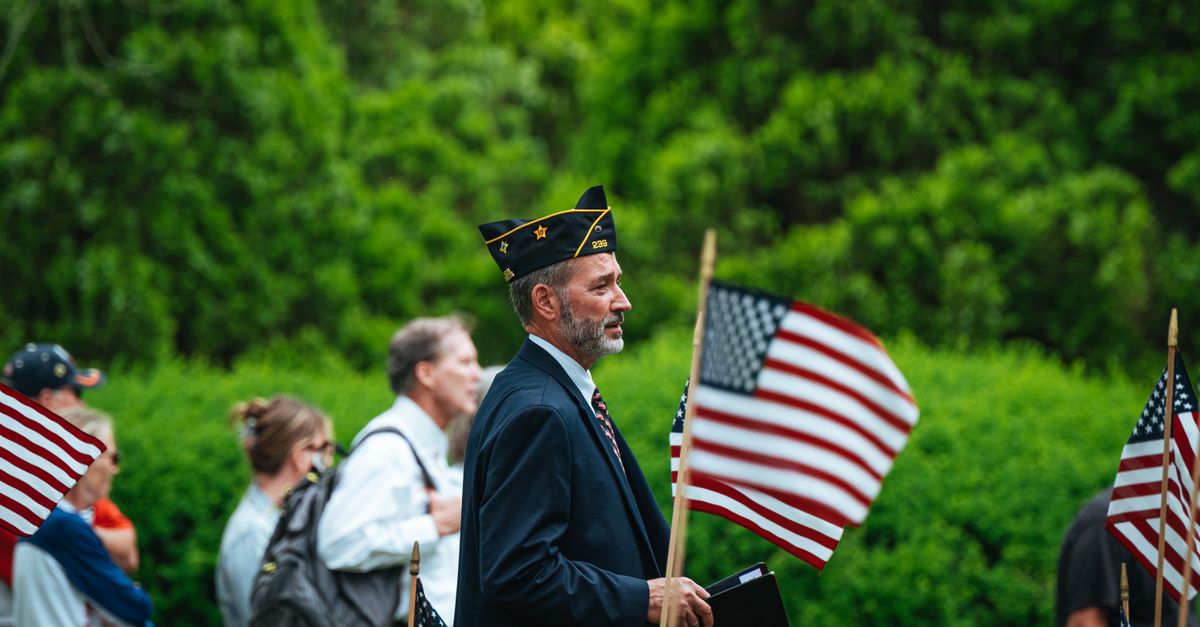 A veteran in a service cap carrying an American flag at an outdoor gathering