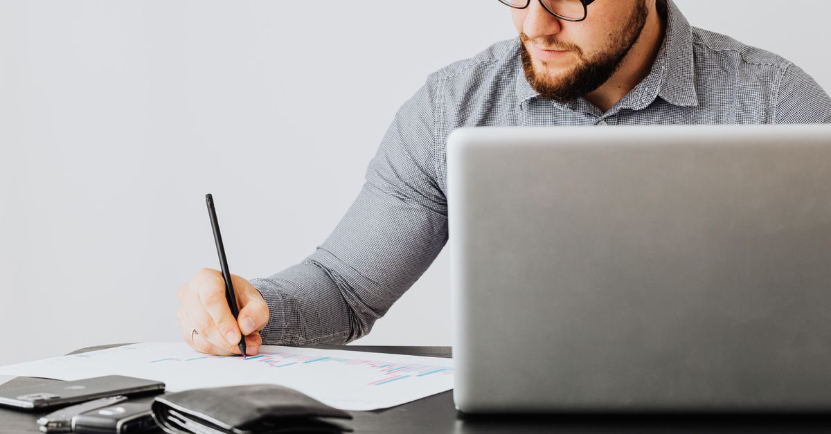 A man writing in a notebook beside a laptop