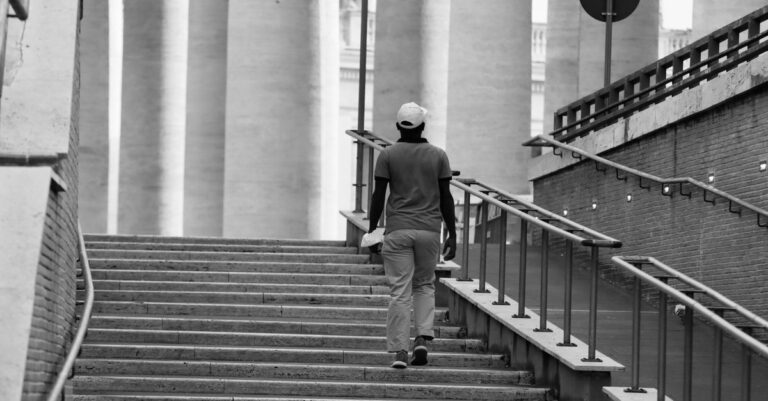 A person climbing a long flight of concrete steps, in black and white