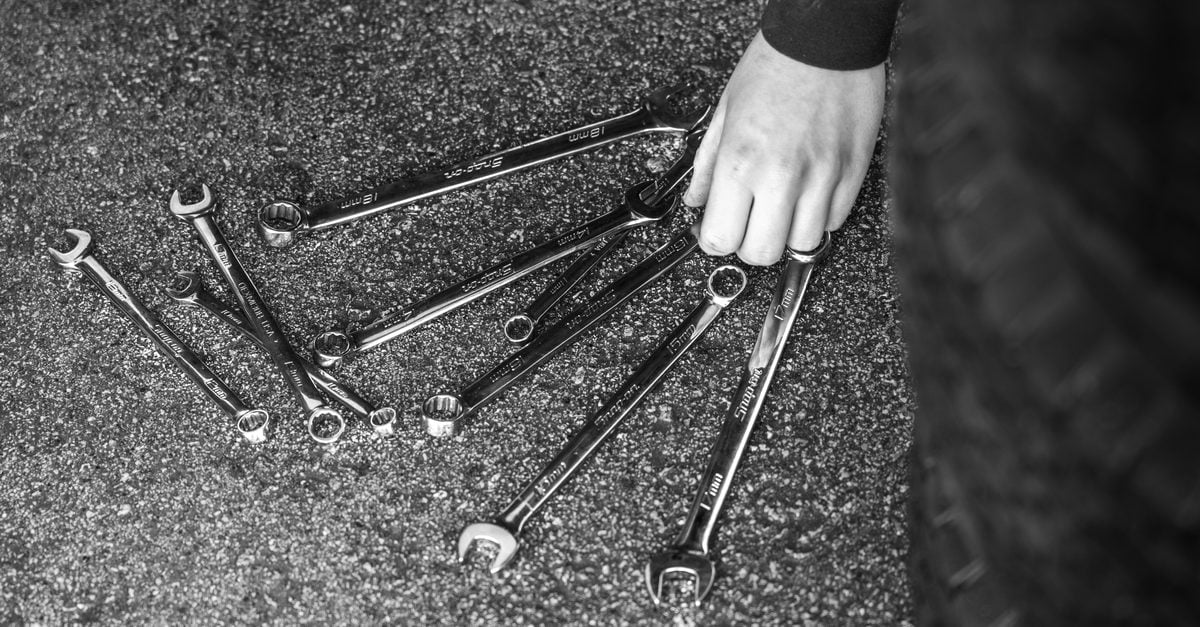 Black and white image of wrenches spread on asphalt with a hand picking up one.