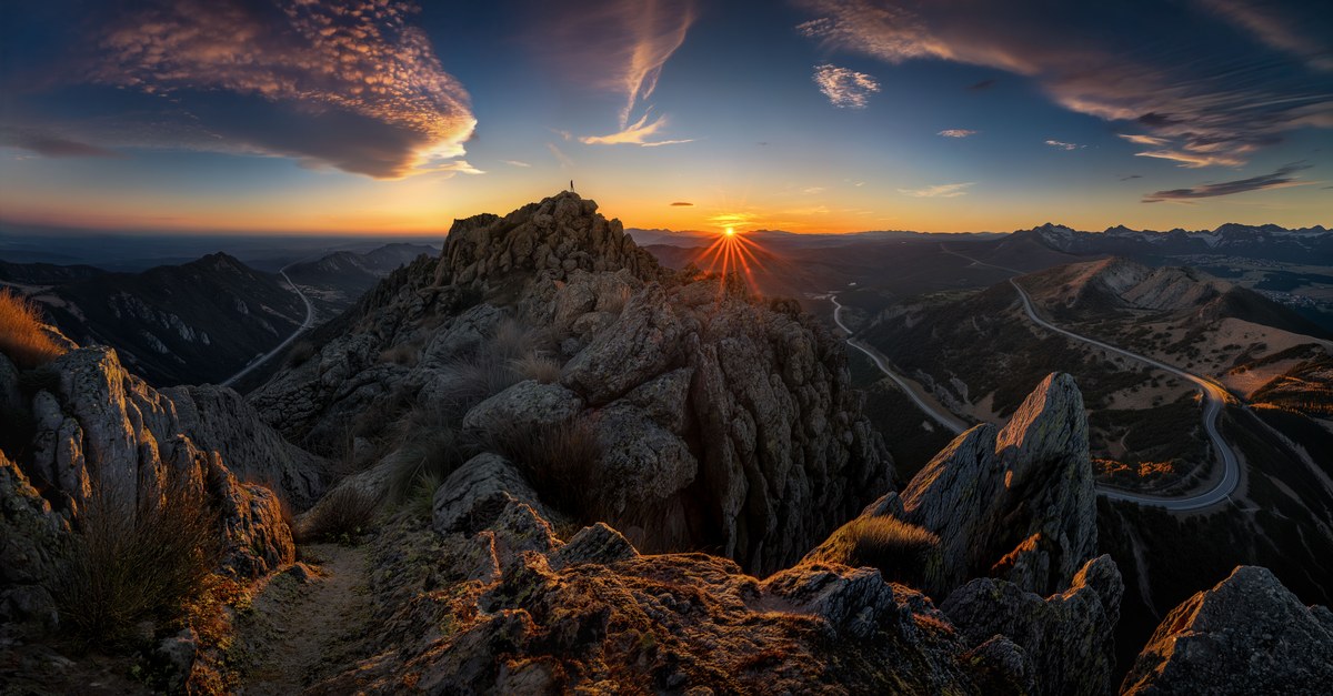 Dramatic sunrise over rugged mountain peaks with a scenic view of winding roads.