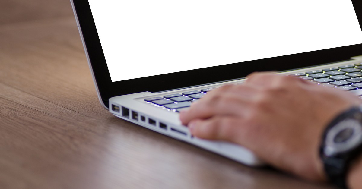 Close-up of a hand using a laptop with a blank screen, ideal for adding custom content.