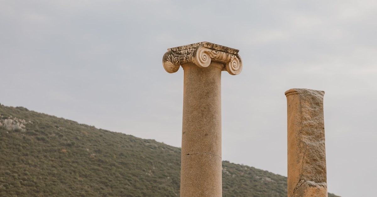 Two ancient columns stand majestically against a serene hillside backdrop.