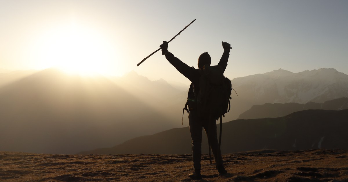 A lone backpacker raises arms triumphantly at sunrise on a mountain peak.
