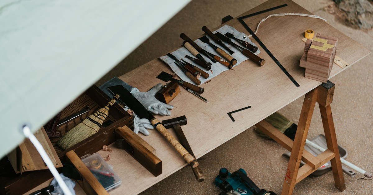 Woodworking chisels, a mallet, and a handsaw laid out on a plywood workbench on sawhorses