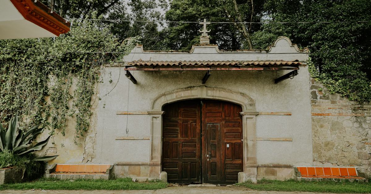 Dark wooden double doors set in a whitewashed stone wall under a small tiled roof, ivy climbing the wall on one side